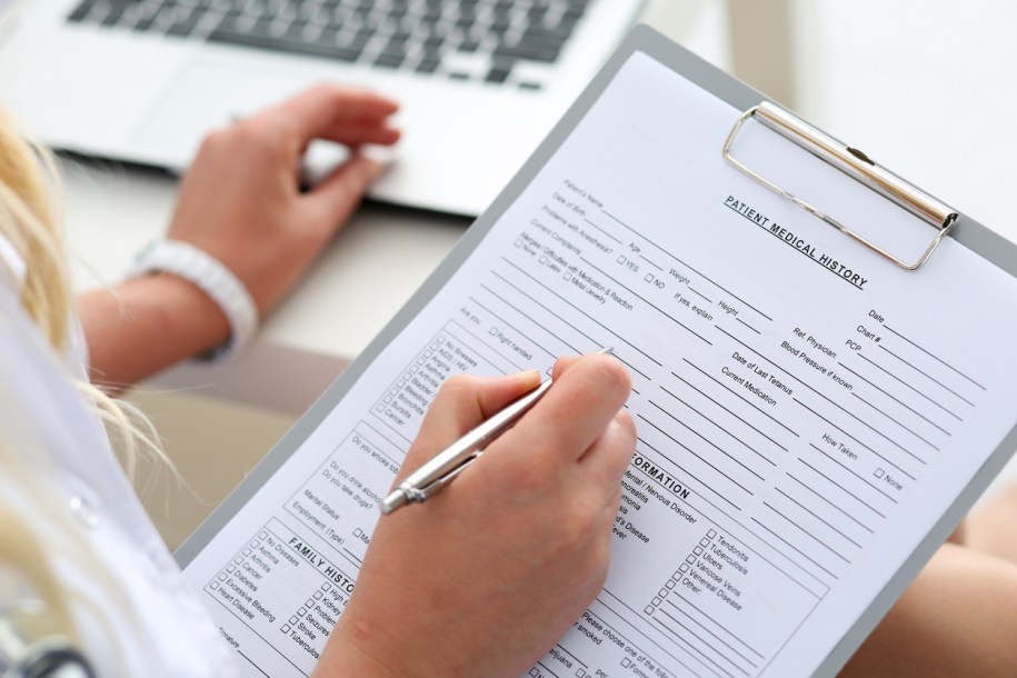 Female doctor hold clipboard pad and fill medical history list with silver pen.