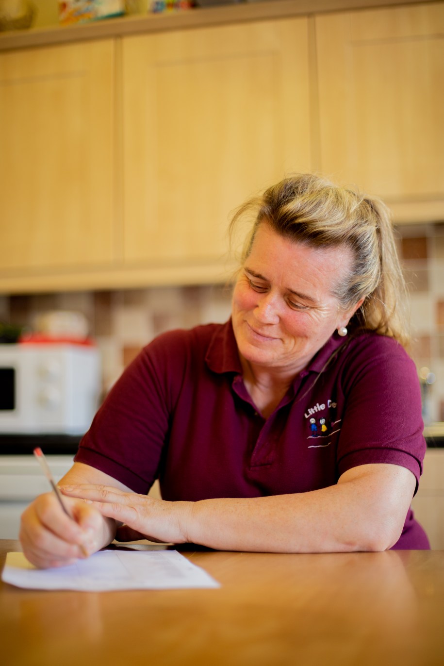 Woman in the kitchen seated at a table is writing on a workbook
