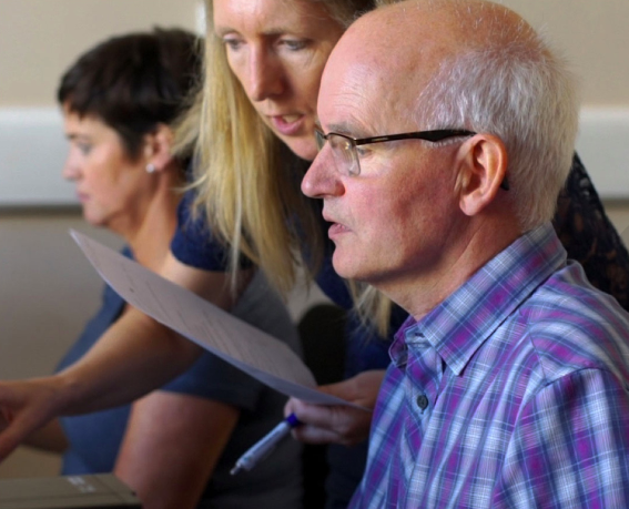 Adult literacy learner sit on a desk while a tutor explains how to use a PC tool