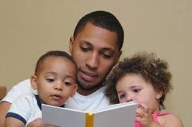Father reading a book and 2 children listening beside him