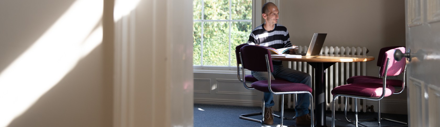 Man seated on a round table reading a workbook in an office