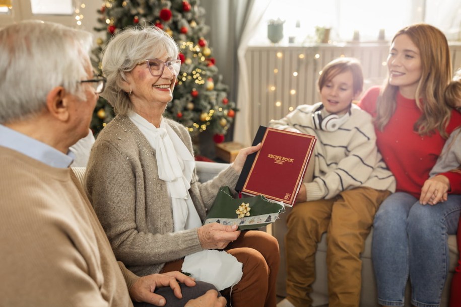 People around Christmas tree with grandparents - Woman holds recipe book