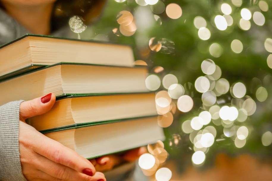 Woman carrying a stack of books behind a Christmas tree