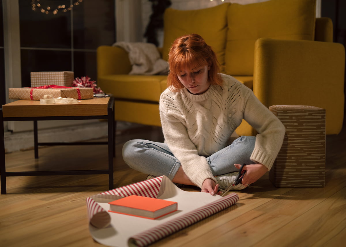 Woman in living room wrapping a book as Christmas gift